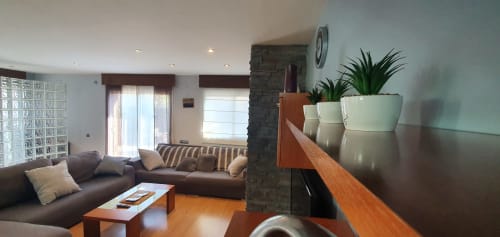 Sala de estar moderna en Villa Castelló Salou con sofá de cuero marrón, mobiliario de madera, plantas en macetas y chimenea de piedra