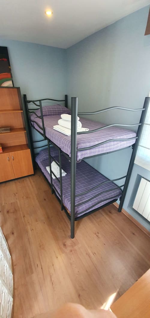 Cama litera de metal con ropa de cama púrpura y toallas blancas en habitación de huéspedes con paredes azules del hotel Villa Castelló Salou en Salou, España