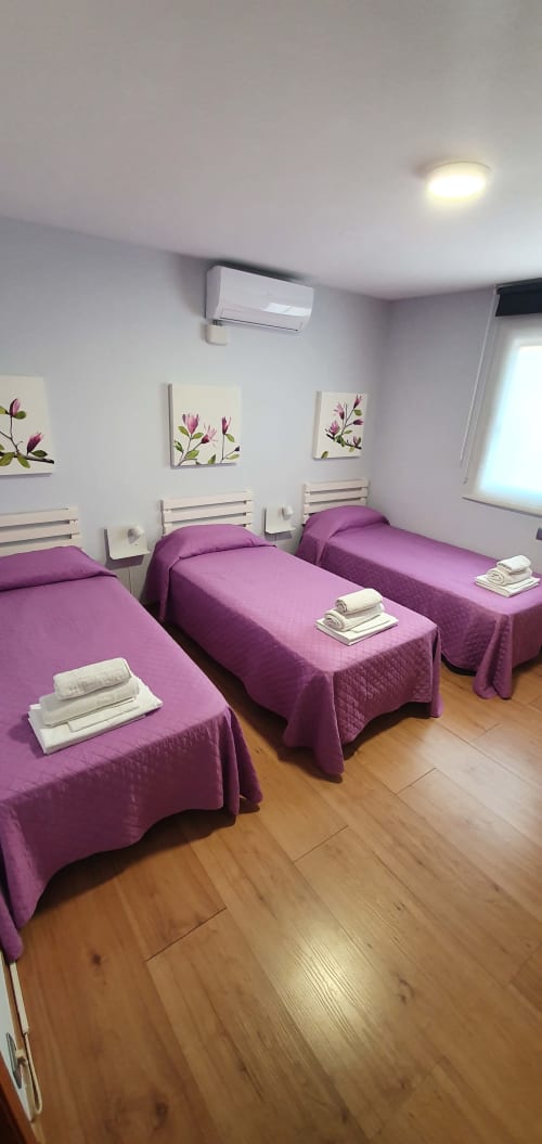 Dormitorio triple en Villa Castelló Salou con camas moradas, cabeceros blancos, piso de madera y arte floral en las paredes