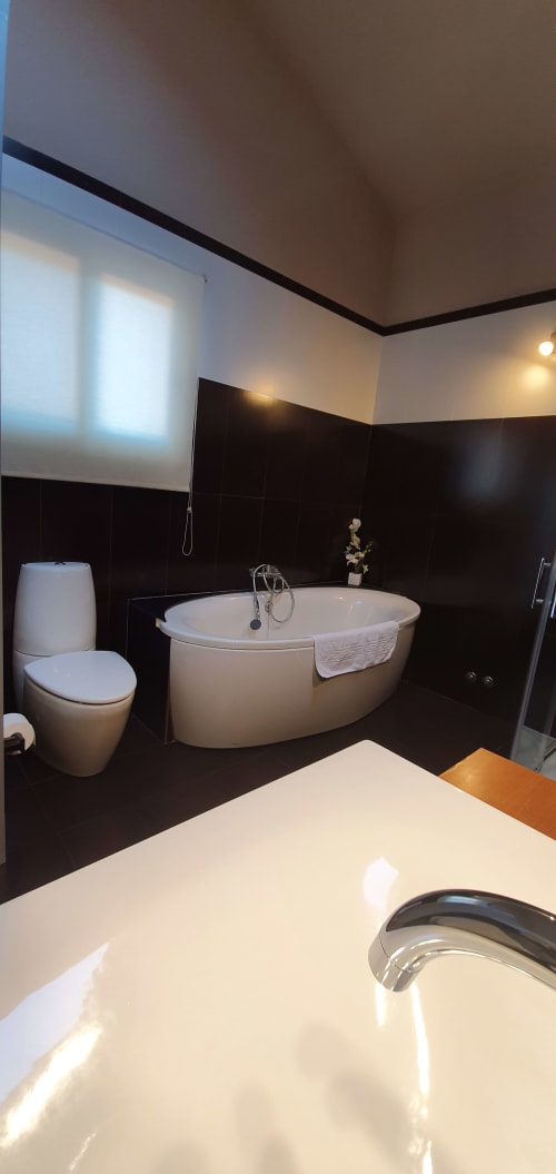 Baño moderno en Villa Castelló Salou con bañera ovalada blanca, inodoro y paredes de azulejos oscuros