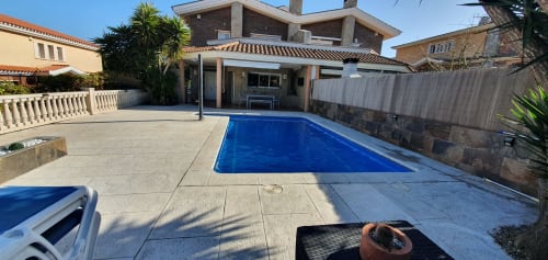 Área de piscina de Villa Castelló Salou con piscina rectangular azul, patio cubierto y terraza de piedra bajo el sol mediterráneo