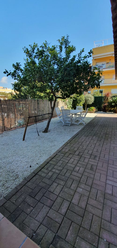 Patio ajardinado de Villa Castelló Salou con árbol, zona de descanso y edificio amarillo