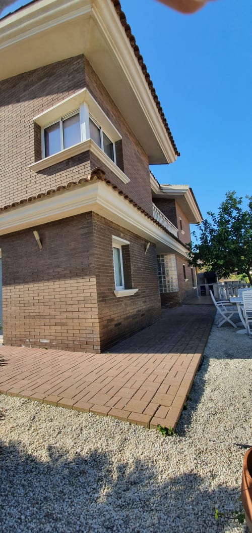 Fachada de ladrillo de Villa Castelló Salou con terraza de madera, molduras blancas y vistas al cielo despejado