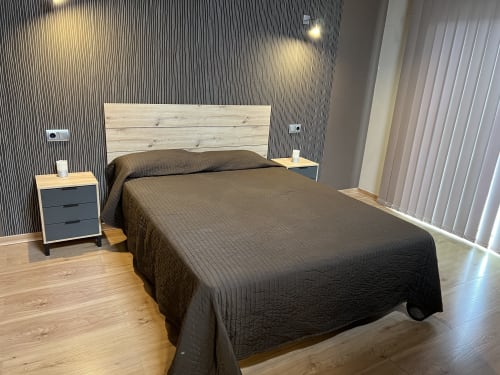 Dormitorio moderno en Villa Castelló Salou con ropa de cama oscura, cabecero de madera clara y panelado contemporáneo en las paredes