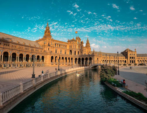 Plaza de España con edificios renacentistas dorados, canal y bandera española en Sevilla