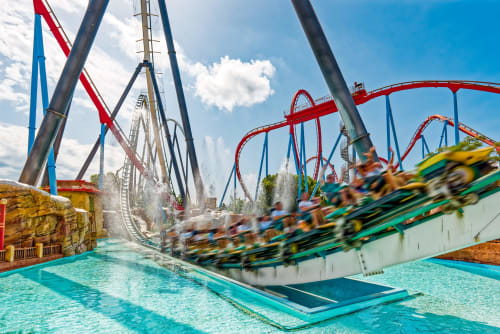 Colorida montaña rusa con vías rojas y azules salpicando el agua turquesa del parque de atracciones de Salou