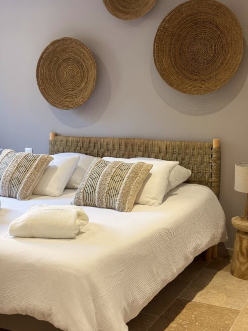 Camera da letto con arte murale circolare intrecciato, testiera in fibre naturali, cuscini rigati e biancheria color crema a Villa Grignan