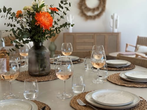 Tavolo elegantemente apparecchiato a La Maison D'ambrine con fiori arancioni, calici di vino e tovagliette intrecciate a Chamaret.