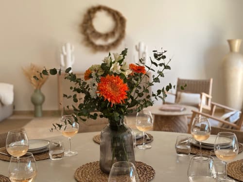 Tavolo elegante a La Maison D'ambrine con gerbere rosse, bicchieri di vino e tovagliette rustiche