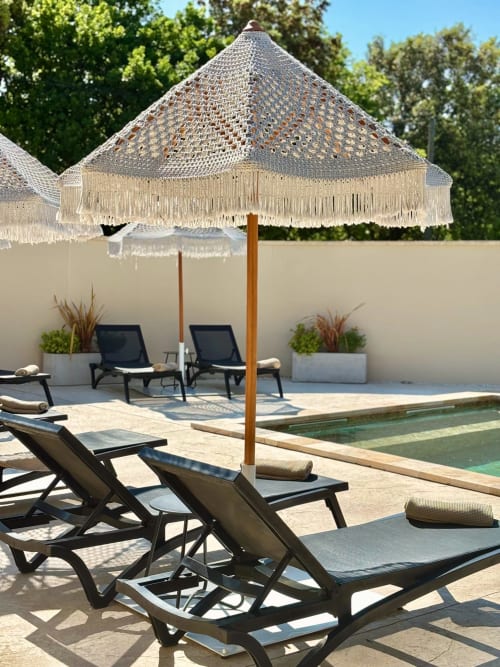 Area lounge a bordo piscina della Maison D'ambrine con ombrellone frangiato, sdraio nere e alberi verdi a Chamaret