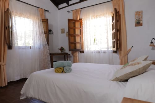 Dormitorio luminoso en Casonas de Marengo con cama blanca, ventanas de madera, cortinas translúcidas y decoración rústica en Icod de los Vinos