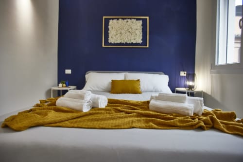 Letto moderno con cuscini bianchi, coperta giallo senape e asciugamani arrotolati presso L.H.A. srl a Ferrara