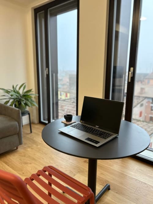 Spazio di lavoro moderno in hotel a Ferrara con laptop al tavolo rotondo, vista sulla città dalle porte-finestre del balcone