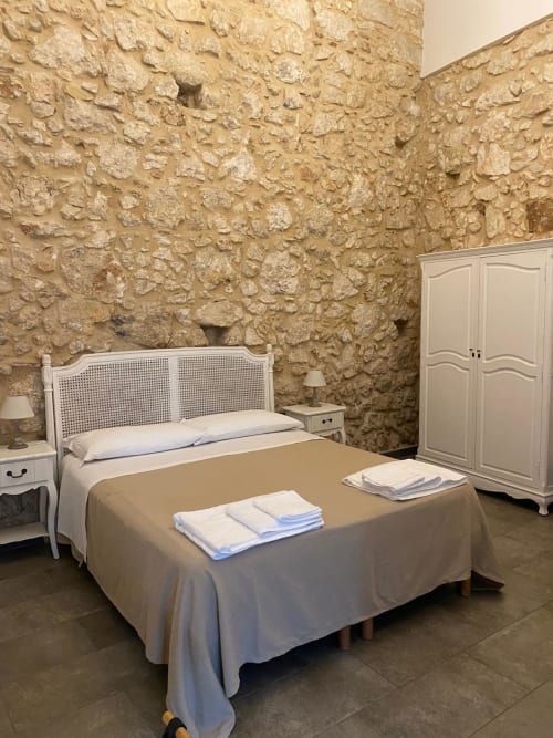 Camera da letto a Corte Sicula B&B a Siracusa con muri in pietra, letto bianco, armadio e fascino rustico