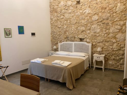 Camera rustica a Corte Sicula B&B a Siracusa con muri in pietra, letto in rattan bianco e arredi tradizionali