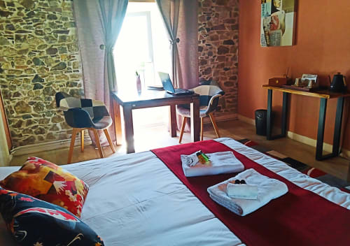 Chambre d’hôtes confortable avec lit double, mur en pierre apparente et petit bureau, dans une ambiance rustique chic en Normandie.