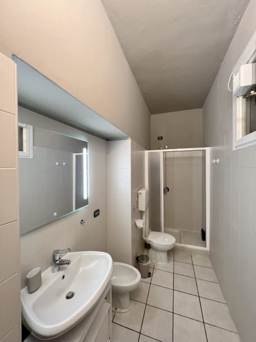 Modern private bathroom at Varenna by Foot with white sink, toilet, shower enclosure, and illuminated mirror