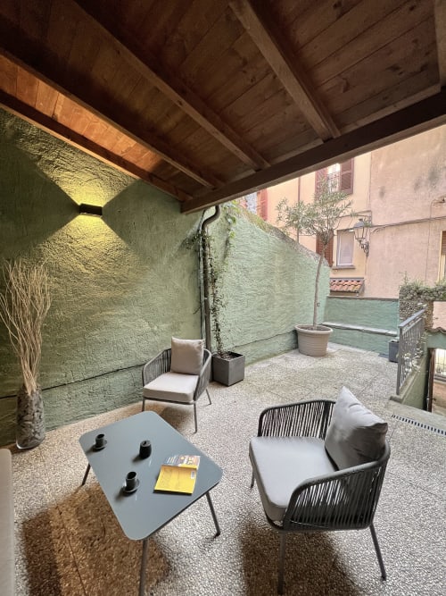 Varenna apartment courtyard with seating area, green walls, wooden beams, potted plants, and modern furniture