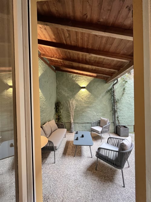 Varenna apartment courtyard with wooden pergola, comfortable seating, small table, and potted palm tree