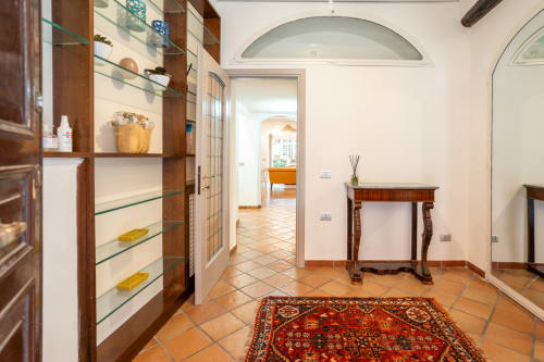 Elegant foyer with terracotta floors, wooden display shelving, ornate console table, and red patterned rug in luxury