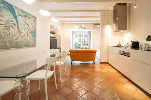 Modern luxury apartment kitchen and living area in Roma with orange sofa, white dining chairs, and terracotta tile flooring