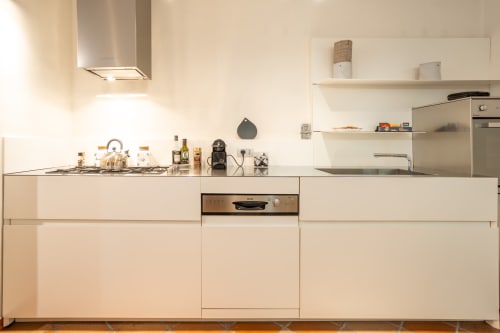 Modern kitchen in luxury Trastevere apartment with white cabinetry, stainless steel appliances, and open shelving