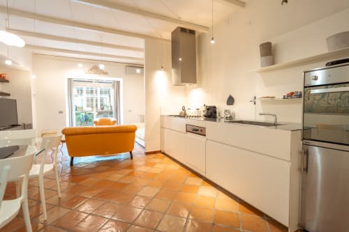 Modern open-plan kitchen and living area in Casa Verde luxury apartment, Rome, with orange terracotta tiles, white cabinetry,