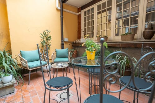 Cozy courtyard patio at Casa Verde luxury apartment in Rome's Trastevere with turquoise chairs, potted plants, and wrought