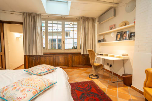 Bright luxury apartment bedroom in Rome's Trastevere with twin beds, wooden desk, built-in shelving, and terracotta floors