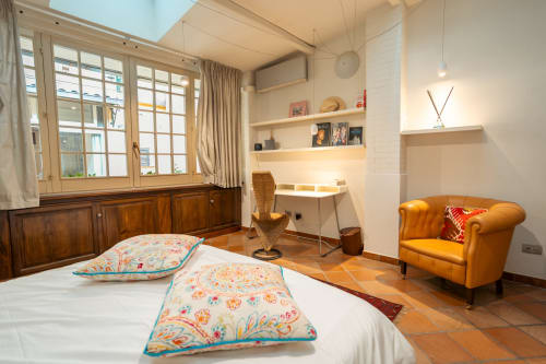 Luxury bedroom in Casa Verde Trastevere apartment with bed, cognac leather armchair, wooden desk, and city views