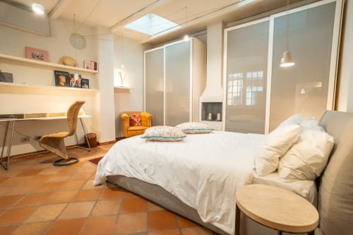 Modern bedroom in luxury Rome apartment with white bed, orange floor, desk, and glass-paneled wardrobe