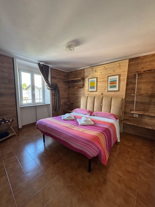 Spacious wooden bedroom in Sormano apartment with colorful striped bedding, mountain views, and tiled flooring