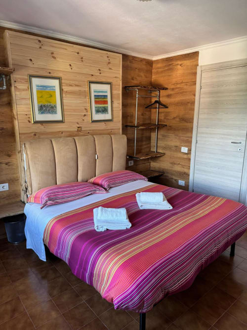 Spacious bedroom in Sormano apartment with striped bedding, wooden walls, framed artwork, and mountain view at THE V