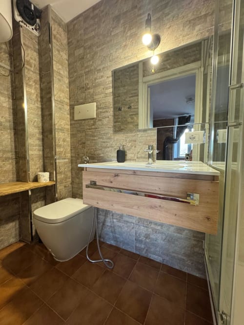 Modern bathroom in Sormano apartment with marble tiles, wooden vanity, mirror, toilet, and shower enclosure