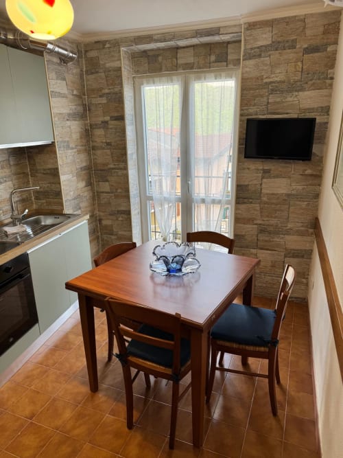Modern kitchen-dining area in Sormano apartment with wooden table, stone tile walls, and balcony doors with mountain view