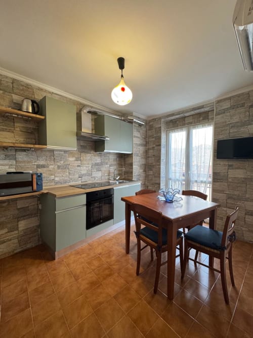 Modern kitchen with dining area in Sormano apartment, featuring wood cabinets, stone backtile, and mountain views