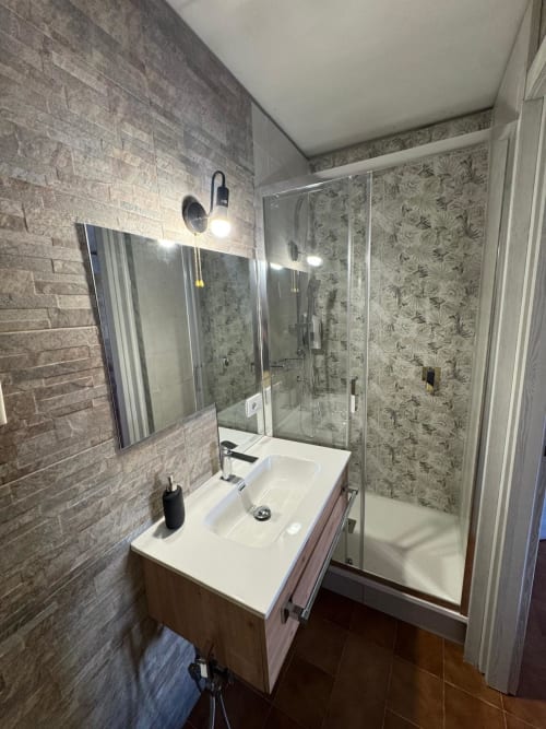 Modern bathroom in Sormano apartment with sink, mirror, glass shower enclosure and tile walls