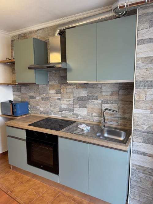 Modern kitchen in Sormano apartment with light blue cabinets, wooden countertop, stainless steel sink, and stone backtile