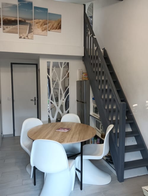 Salle à manger de villa moderne avec table ronde en bois, chaises blanches et escalier noir au gîte de Feyzin