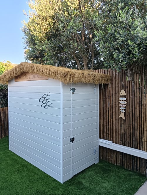 Petit abri de jardin blanc au toit de chaume du Gîte des Gônes à Feyzin, entouré d'une clôture en bois et d'oliviers