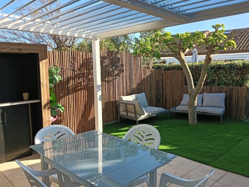 Jardin de villa moderne au Gîte des Gônes avec terrasse, salon extérieur, pergola, gazon synthétique et clôture en bois