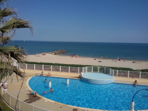Piscines en bord de mer avec clients, plage de sable et voiliers au Gîte des Gônes à Feyzin