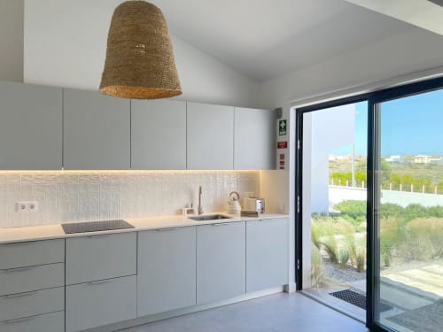 Cozinha moderna na Villa Casa Beliche, Bordeira. Armários cinza claro, azulejaria branca, vista para o mar pela porta de vidro