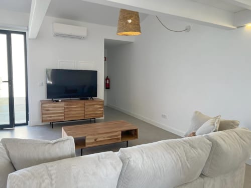 Sala de estar moderna da villa Casa Beliche em Bordeira com sofá creme, painel de TV em madeira e vista para o mar pelas portas de vidro