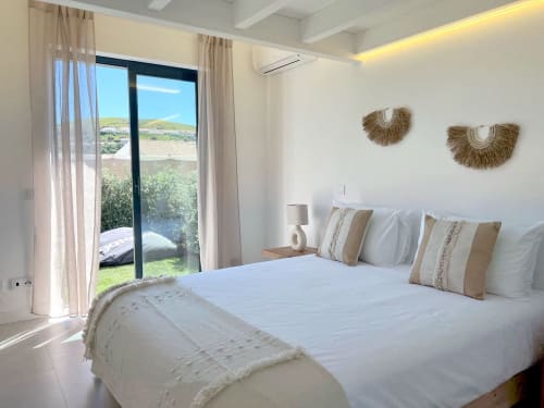 Bright modern bedroom at Casa Telheiro villa in Bordeira with sea view, white bedding, woven wall art, and garden access