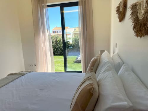 Quarto luminoso da villa Star Host em Bordeira com almofadas brancas, vista para o jardim através das portas de vidro e arquitetura costeira