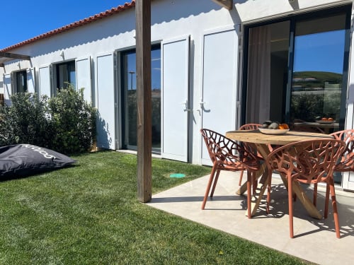 Pátio da villa Casa Telheiro com mesa de jantar, edifício branco moderno, gramado verde e vista para o mar em Bordeira, Portugal