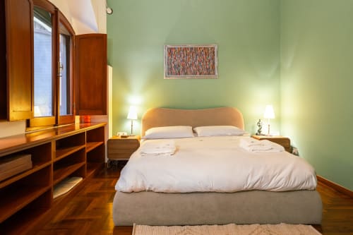 Elegante camera da letto in studio a Roma con pareti verde salvia, arredi in legno, biancheria bianca e pavimento in parquet
