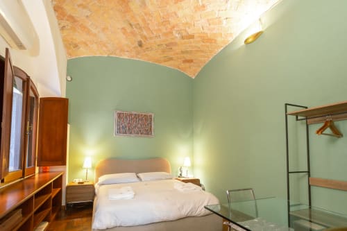 Elegante monolocale a Roma con pareti verde salvia, soffitto in legno, letto con comodini e moderni comfort inclusi