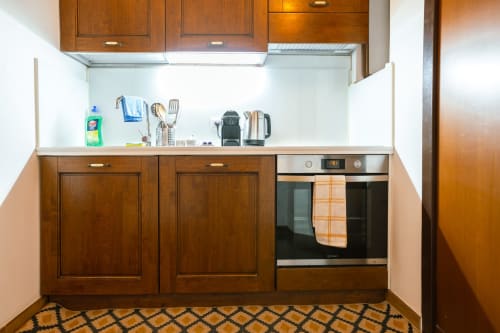 Cucina compatta in studio con mobili in legno, forno in acciaio inox e piano di lavoro bianco in appartamento romano